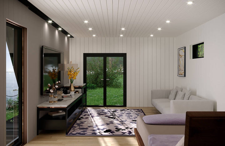 Interior of glamping unit featuring a white sofa, flat-screen TV, floral rug, and double glass doors opening to a grassy outdoor view.