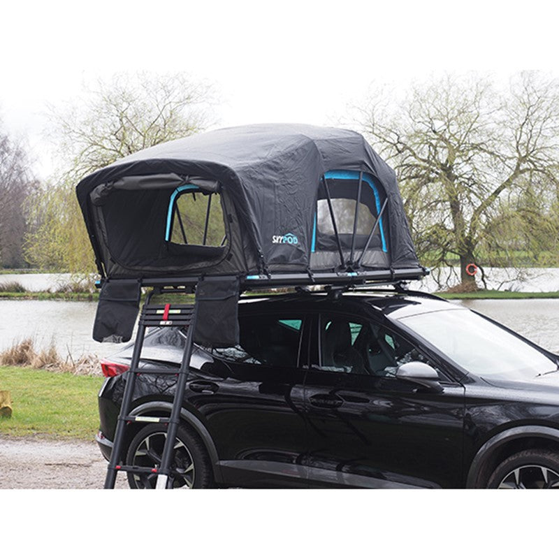 Skypod Lite rooftop tent mounted on a black SUV parked beside a lake in a countryside campsite.