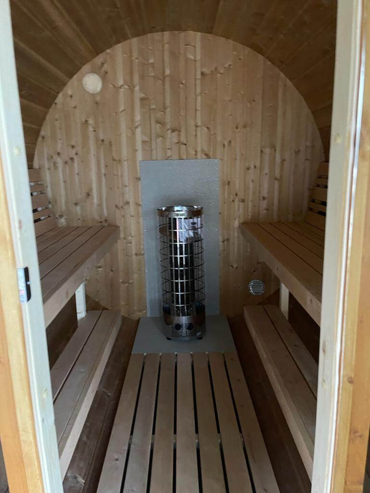 Interior view of InMedias Barrel Sauna 280 Deluxe showing twin benches and a central electric heater, natural wood finish.