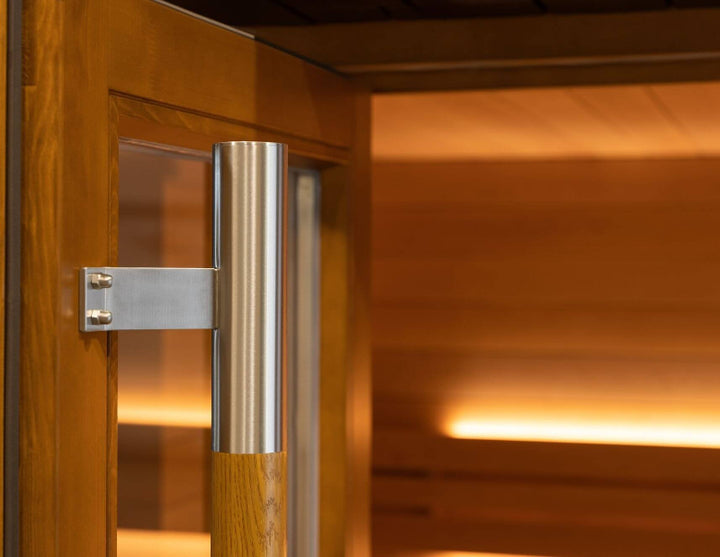 Close-up of the Saunum AirCube Space sauna door handle, made of brushed stainless steel and wood, attached to a glass-paneled wooden door.