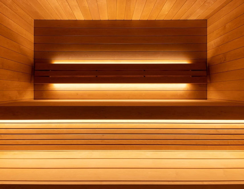 Interior view of the Saunum AirCube Space sauna showing tiered wooden bench seating with ambient LED strip lighting.