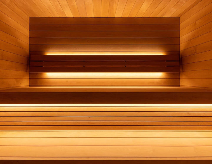 Interior view of the Saunum AirCube Space sauna showing tiered wooden bench seating with ambient LED strip lighting.