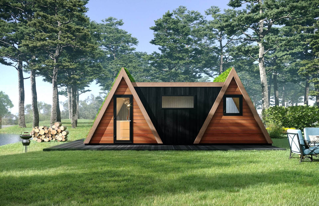 Front view of double A-frame glamping cabin with green roofs and mixed timber cladding, surrounded by trees, lake, and outdoor seating.