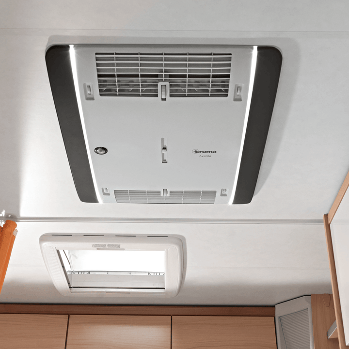 Interior ceiling-mounted Truma Aventa Comfort unit in white, installed in a caravan, showing vent grills and control layout.