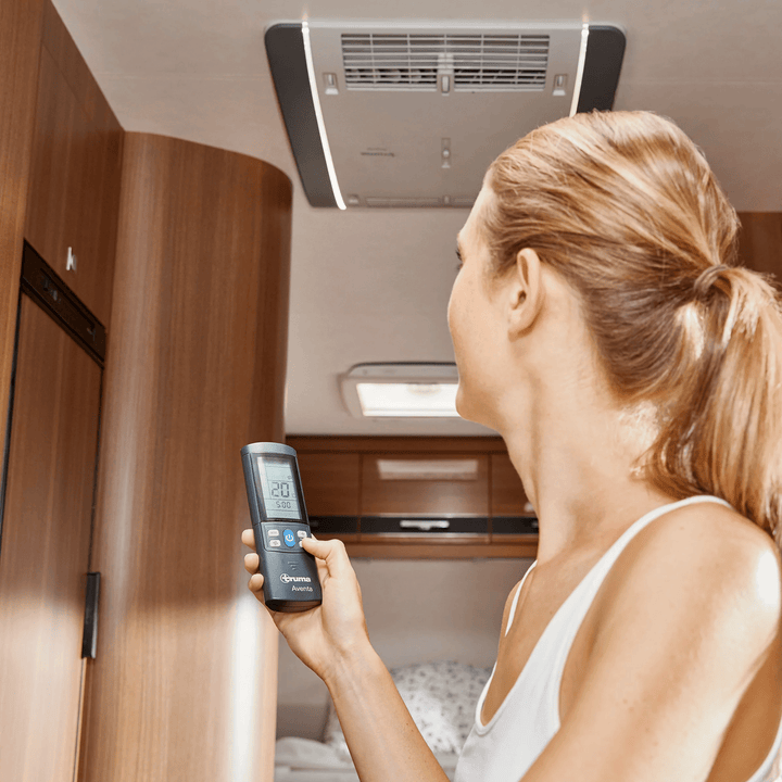 Woman standing inside a caravan controlling the Truma Aventa Comfort ceiling unit with a remote control.