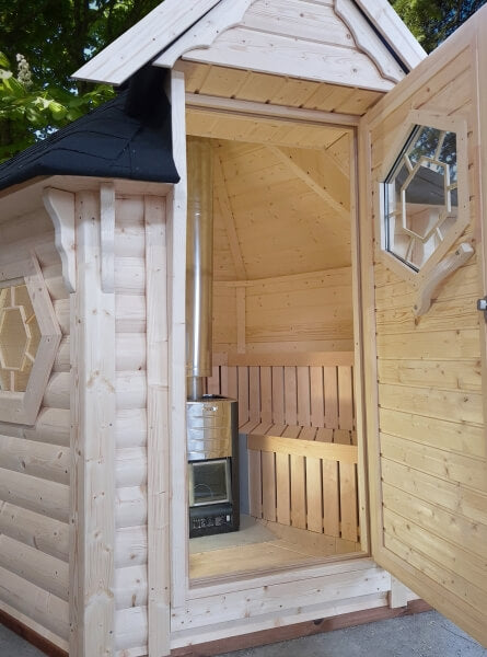 Open door view of Viking Industrier sauna cabin 4.5m² showing wooden interior and stove, on a shaded forest background.