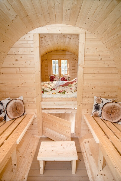 Interior of a Viking Industrier 2.2 x 4m Sleeping Barrel showing twin benches with pillows and a central door leading to a floral-themed bedroom.