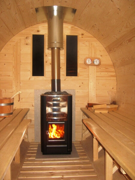 Inside view of a Viking Industrier Barrel Sauna 1.9 x 3.5m showing a lit stove and wooden benches, on a warm indoor background.