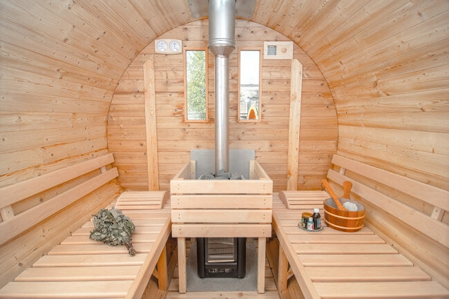 Interior view of Viking Industrier Barrel Sauna 2.2 x 4m featuring light wood benches and a central wood-burning stove.