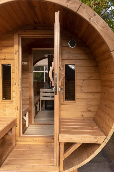 Open door view of a Viking Industrier Barrel Sauna with terrace, revealing the entrance and interior benches, in an outdoor setting with sunlight.