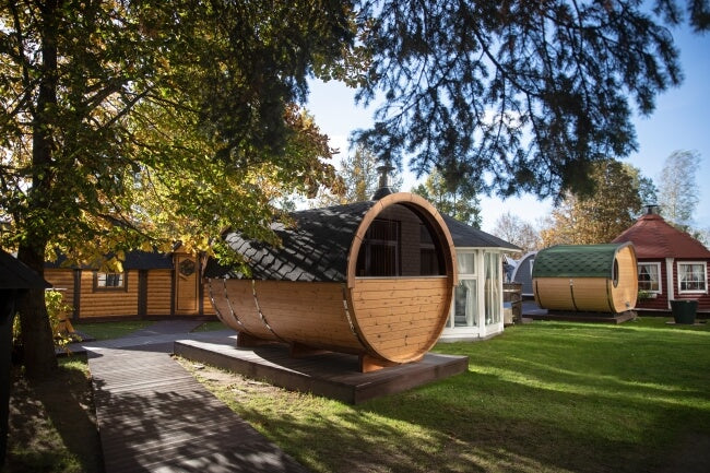 Rear angled view of multiple Viking Industrier Barrel Saunas displayed outdoors in a yard under trees, during daytime.