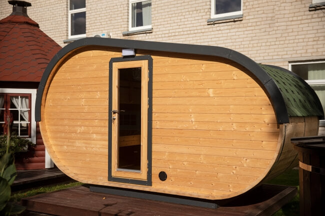 Front side of the Viking Industrier Delight Camping Pod 2.4 x 4.3m with narrow vertical glass door and dark gray roof trim. Located outdoors near a red structure.