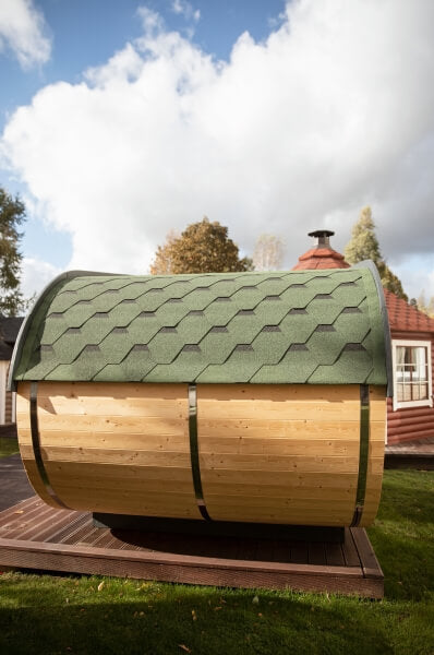 Side view of the Viking Industrier Delight Camping Pod 2.4 x 4.3m with green hexagonal shingle roof and natural wood finish, placed on a wooden deck outdoors. Background shows cloudy blue sky and trees.