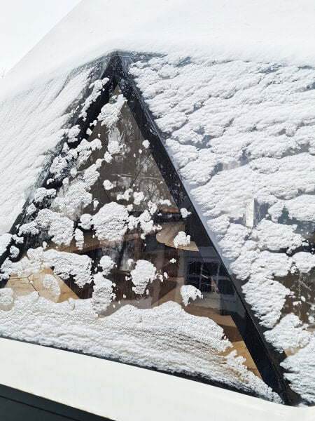 Close-up of a triangular snow-covered transparent window of the Viking Industrier Glamping Dome 10m, viewed from outside.