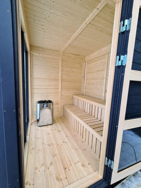 Interior view of Viking Industrier Sauna Cube 2 x 2m featuring a corner heater and tiered wooden bench, taken from the open door.