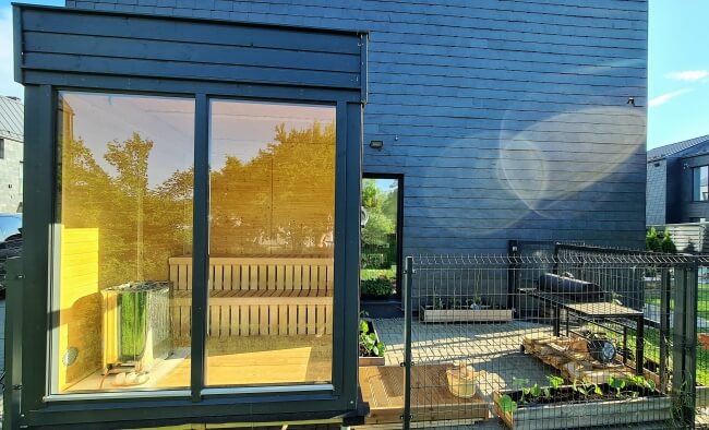 Side view of Viking Industrier Sauna Cube 2 x 2m with dark exterior and large tinted glass wall, placed against a dark modern house.