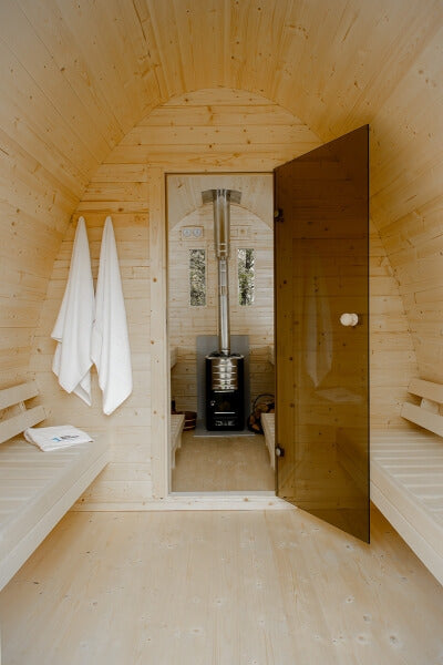 Interior view of Viking Industrier Sauna Pod 2.4 x 4m with glass door and wood stove, light wood walls and benches.