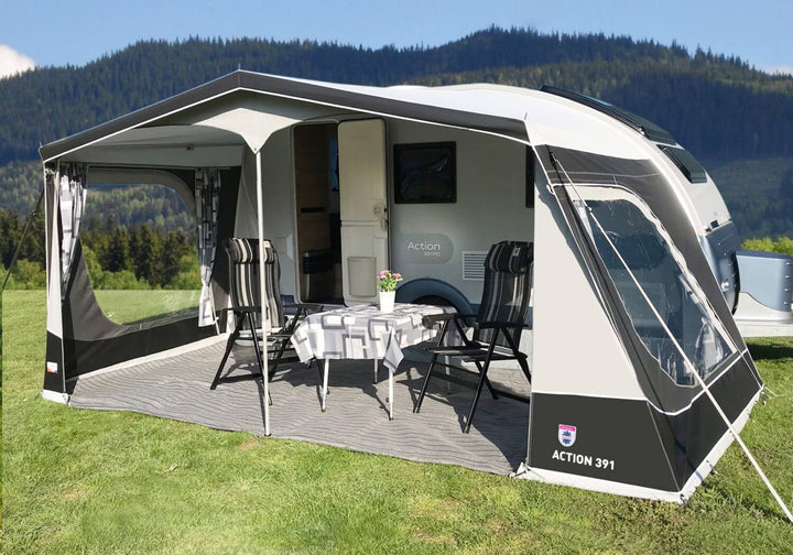 Walker Adria Action 391 awning setup in a grassy field, with chairs and a table arranged under the canopy beside the caravan.