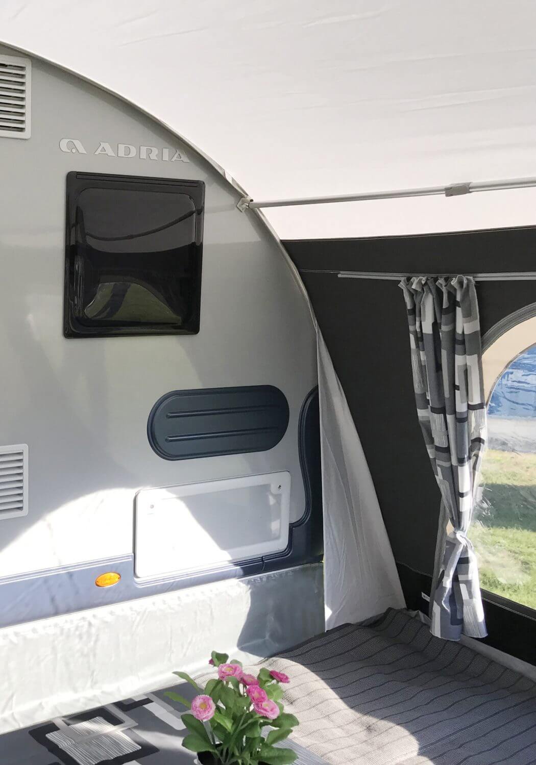 Corner interior of the Walker awning attached to the Adria caravan, featuring curtained window and grey floor mat.