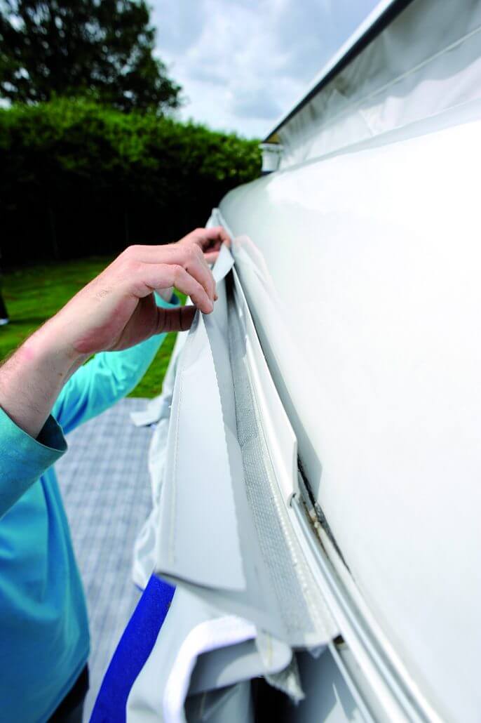 Close-up of a person attaching Walker Eriba awning using velcro and keder strip on a caravan.