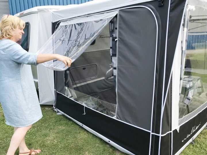 Woman lifting transparent window flap on Walker Touring-Plus awning attached to Eriba caravan.