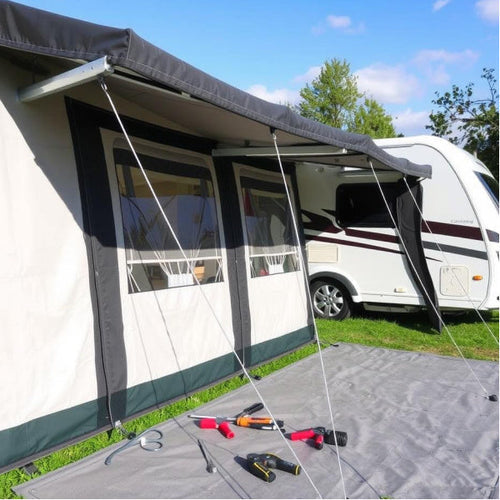 A black awning next to a caravan with tools and a mat on the floor next to it