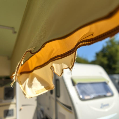 Close up of frayed fabric on a caravan awning, with a caravan in the background