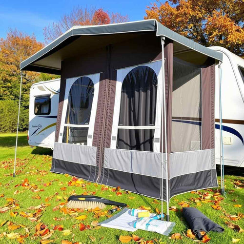 A caravan awning next to a caravan with autumnal leaves and trees behind it