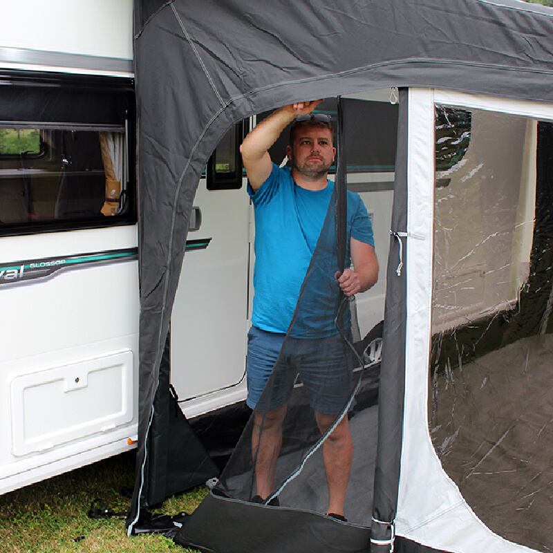 A man setting up a caravan awning by zipping the side in, in front of a caravan