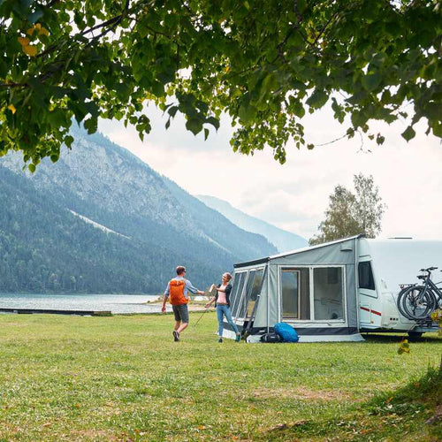 A couple standing outside a caravan awning next to a lake and hill