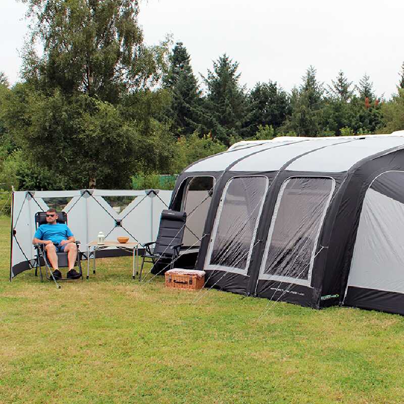 A man sat in a chair next to a windbreak and a caravan awning