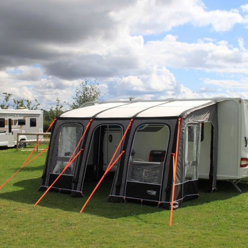 A grey caravan air awning with orange guylines in a field with a cloudy background