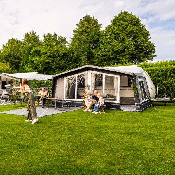 A family in front of a caravan awning with kids playing on the grass
