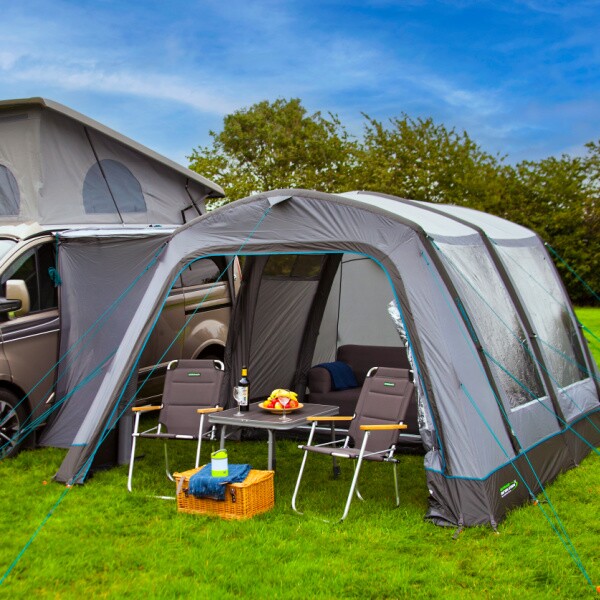 An Outdoor Revolution awning connected to a van in a field, with chairs in front of the awning