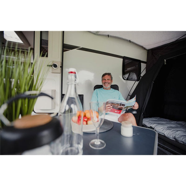 A man sitting at a table inside a Vango awning smiling while holding a magazine