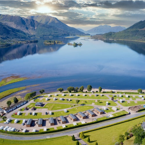 Long distance shot of a campsite with multiple pitches next to a large lake with hills to all sides