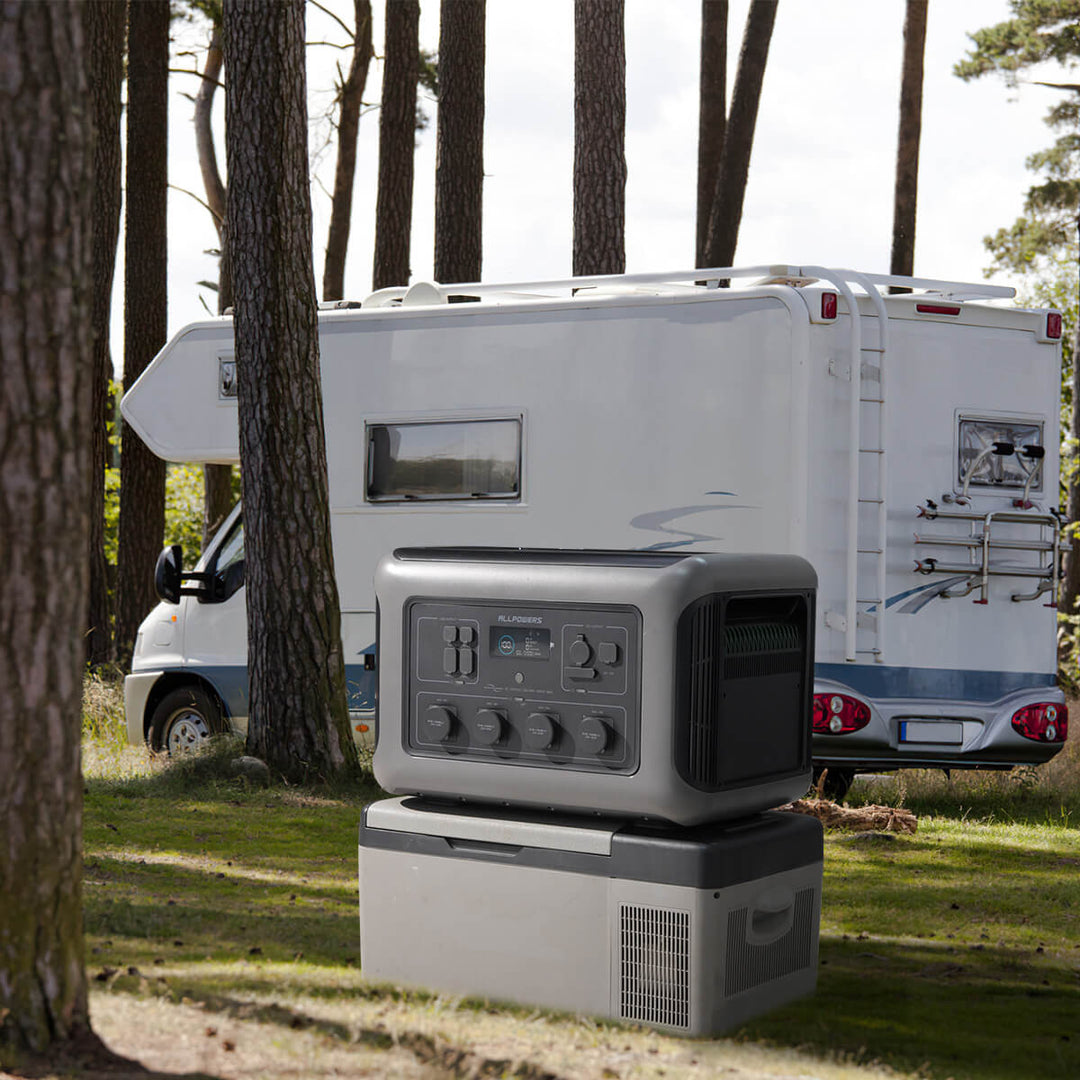 ALLPOWERS R3500 portable power station placed on a portable fridge near a motorhome in a forest campsite.
