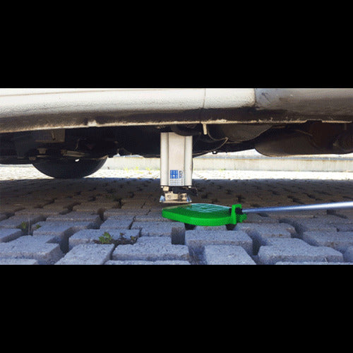 Tesa Autolift4 electric levelling system jack installed under a vehicle with green control tool operating the stabiliser on a paved driveway background.