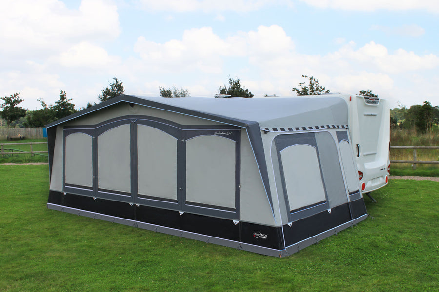 Camptech Buckingham DL full caravan awning attached to a white caravan on green grass under a cloudy blue sky at a campsite.