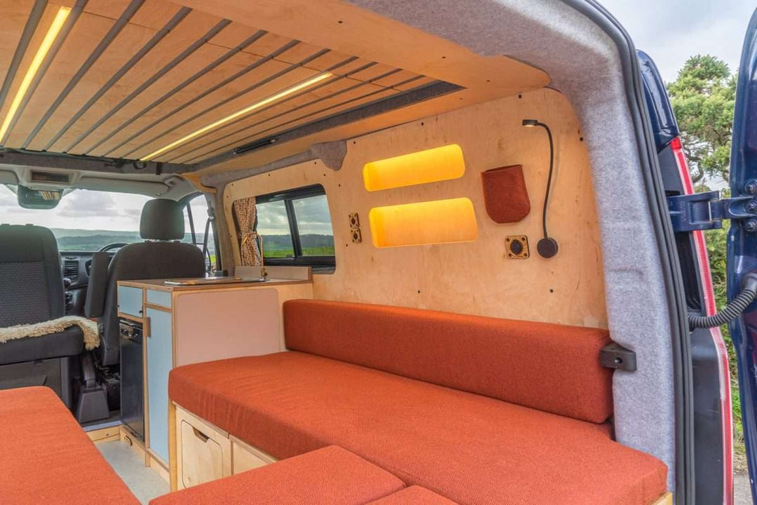 Campervan Bivi L Shaped Bed in burnt orange upholstery installed inside a campervan with wood cabinetry and warm LED wall lights