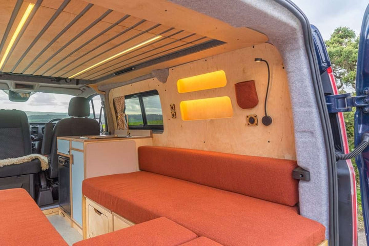 Campervan Bivi L Shaped Bed in burnt orange upholstery installed inside a campervan with wood cabinetry and warm LED wall lights