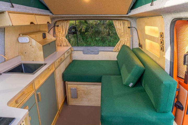 Campervan Bivi L Shaped Bed in moss green upholstery with matching cushions and side storage inside a fully converted campervan.