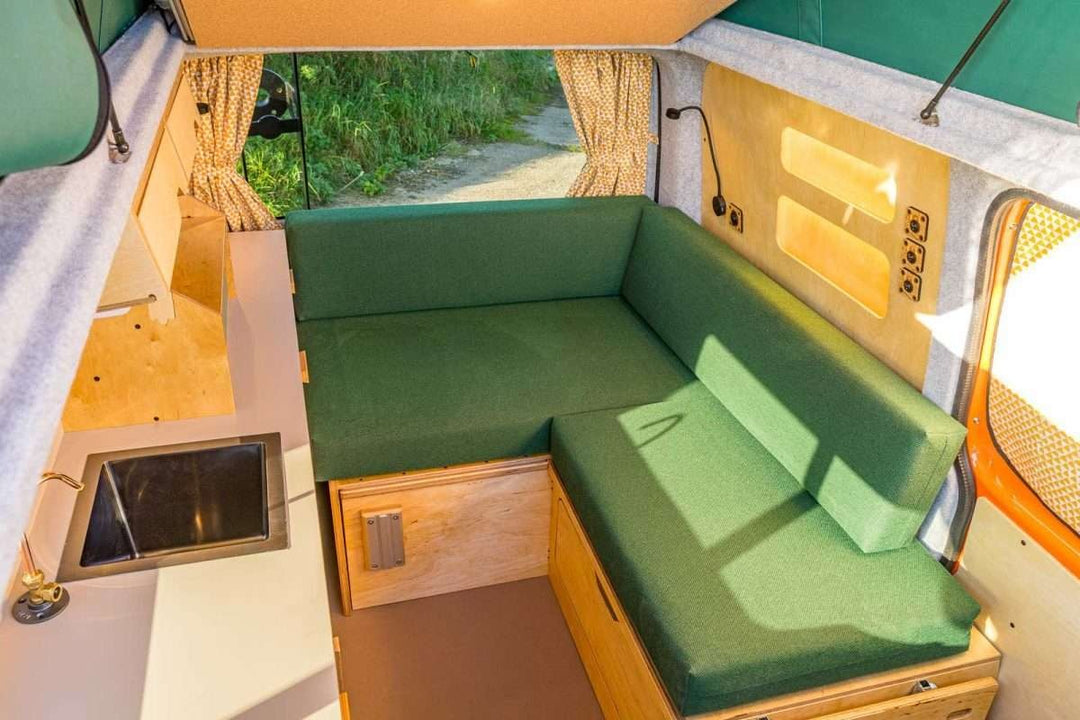 Campervan Bivi L Shaped Bed in olive green fabric configured as a seating area beside a compact sink unit inside a campervan.