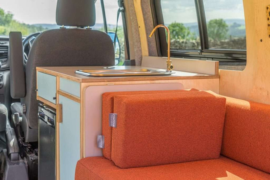 Close-up view of the Campervan Helm Kitchen Unit showing the compact sink, wooden countertop, and orange seating inside a campervan.