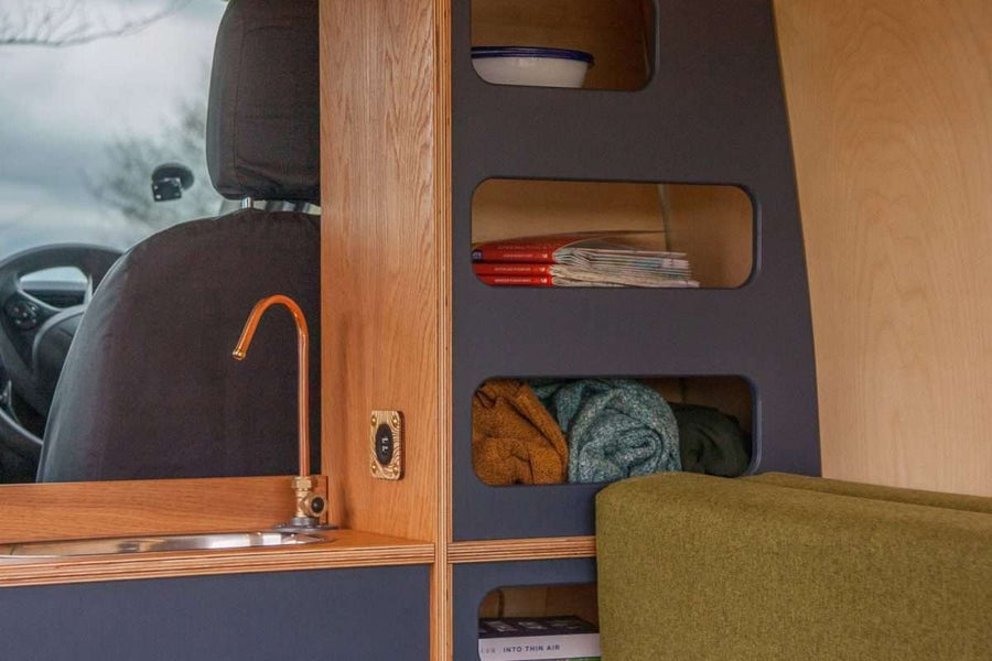 Campervan Navi Kitchen Unit close up of sink with copper tap and open shelving for books and blankets.
