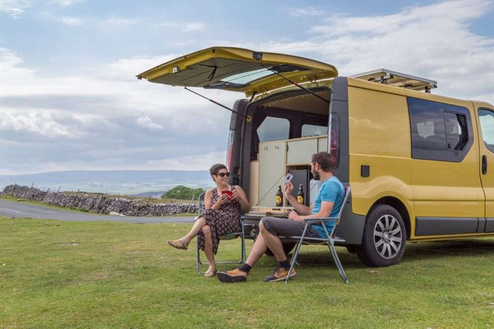 Campervan Ranger Kitchen Unit exterior view with rear hatch open and couple seated at camping table beside a yellow campervan.