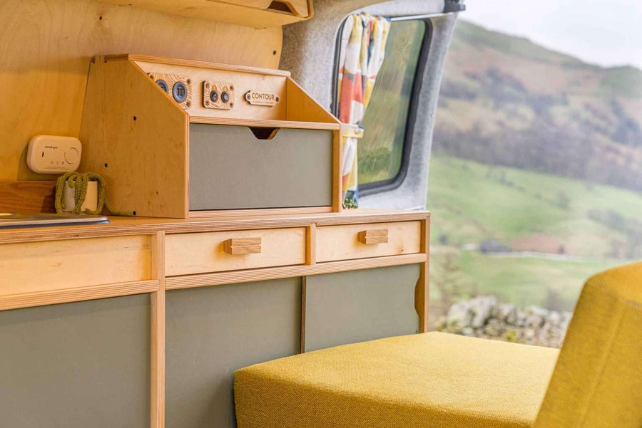Campervan Squall Kitchen Unit side cabinet with drawers and overhead storage inside a campervan, countryside hills visible through the window.