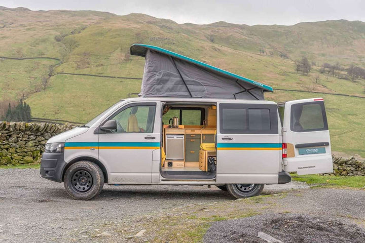 Campervan Squall Kitchen Unit installed in VW Transporter with pop top roof open, side door open on a rural hillside.