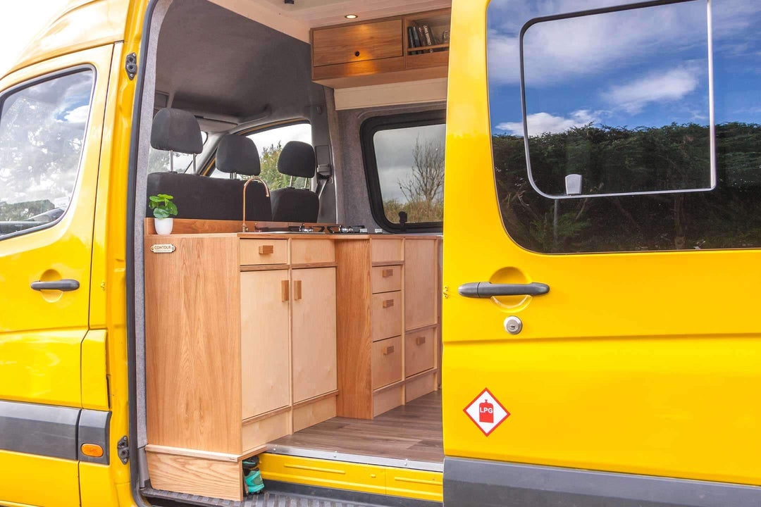 Campervan “Swale” Benches full side installation view inside bright yellow campervan with sliding door open, countryside setting.
