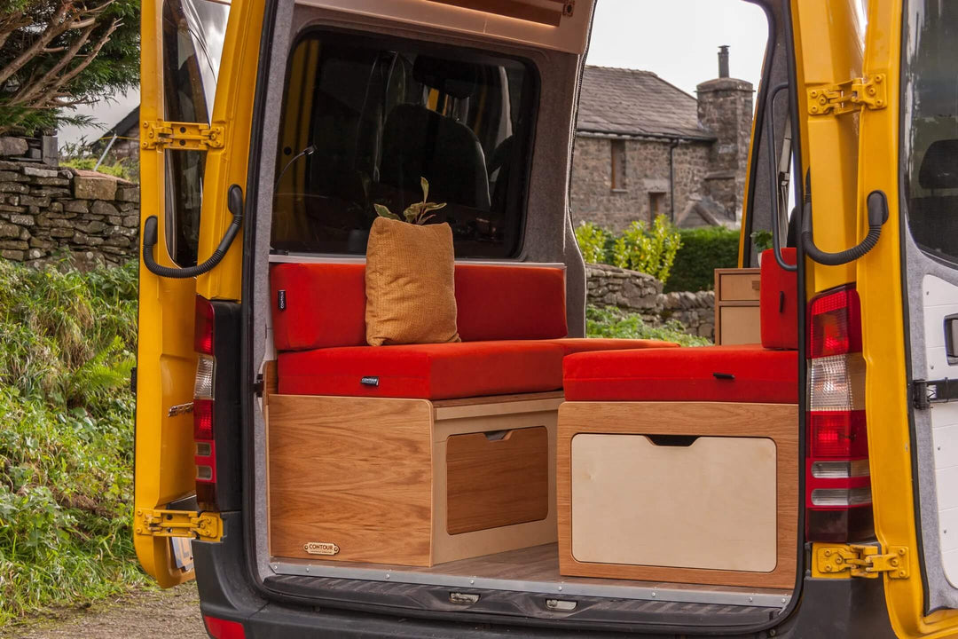 Campervan “Swale” Benches interior layout featuring oak kitchen unit and red bench seating inside yellow campervan, campsite background.